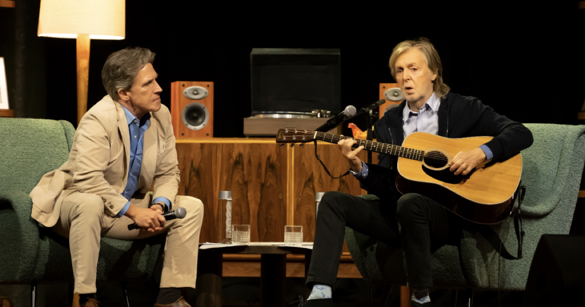 Paul McCartney seated with an acoustic guitar wearing light blue custom socks