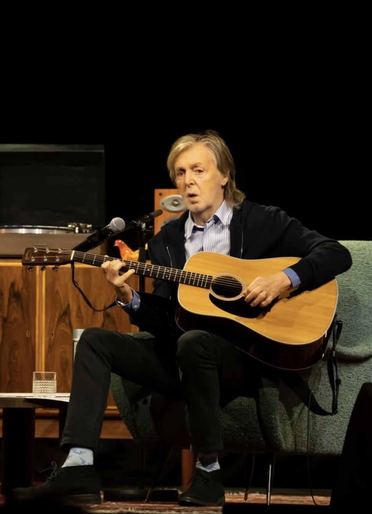 Paul McCartney seated with an acoustic guitar wearing light blue custom socks